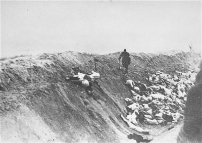 Liepāja, Letland, 1941. Mand skubber et lig ned i en massegrav efter henrettelse ©USHMM