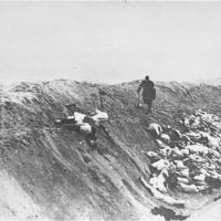 Liepāja, Letland, 1941. Mand skubber et lig ned i en massegrav efter henrettelse ©USHMM